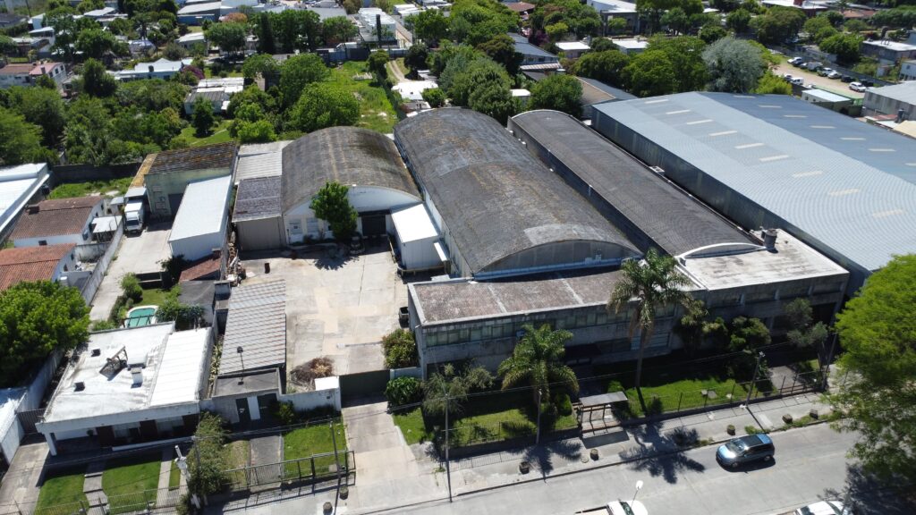 Vista aérea de un amplio complejo de nave industrial y depósito logístico con generosa explanada frontal de maniobras, ubicado en una zona estratégica de Montevideo con excelentes accesos